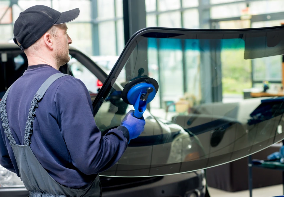 Technicien automobile installant un pare-brise sur véhicule noir dans garage professionnel
