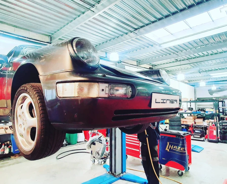 Vue intérieure d'un atelier de carrosserie professionnel moderne montrant un technicien en uniforme effectuant des travaux de réparation carrosserie sur une voiture. L'atelier doit être bien équipé, montrer des outils pneumatiques, des équipements de carrosserie, et l'environnement professionnel doit clairement identifier un atelier automobile spécialisé plutôt qu'un atelier de menuiserie.