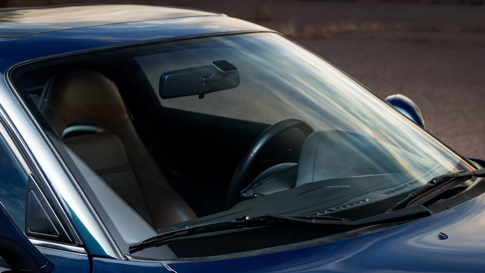 Un technicien spécialisé en atelier automobile moderne, vêtu d'une combinaison de travail professionnelle, en train d'effectuer un diagnostic électronique ou une intervention technique de précision sur un véhicule Porsche ou autre véhicule de prestige, utilisant des équipements de diagnostic professionnels. L'environnement doit montrer un atelier bien équipé avec des outils spécialisés et l'éclairage professionnel d'un garage haut de gamme. Le technicien doit être concentré sur sa tâche, incarnant l'expertise et la maîtrise technique.