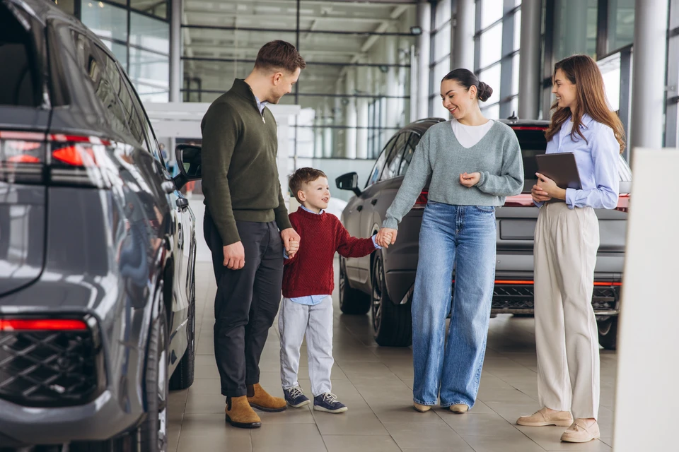 Concession automobile moderne avec vendeur en chemise blanche présentant SUV gris métallisé à cliente potentielle