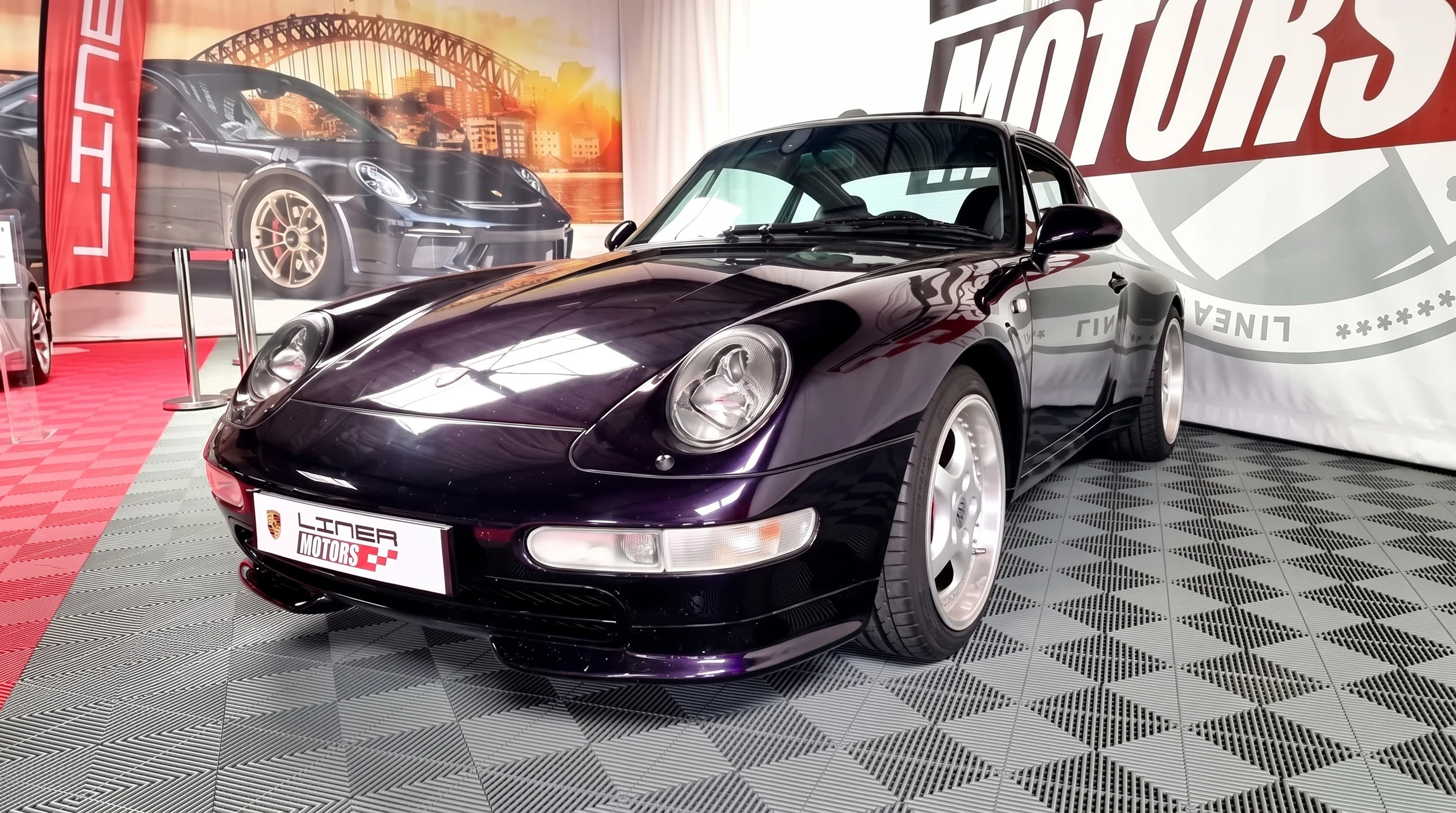 Photographie en couleur d'un atelier de carrosserie professionnel équipé, montrant un technicien spécialisé en tenue de travail effectuant une retouche ou une finition carrosserie de haute précision sur un véhicule de prestige (Porsche, BMW ou Mercedes). L'image doit illustrer le savoir-faire et la qualité du travail : détails de la technique, outils professionnels, éclairage atelier et concentration du technicien. Le contexte doit suggérer expertise et rigueur artisanale.